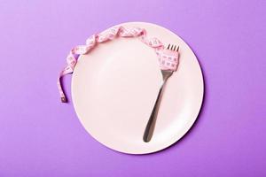 concepto de dieta estricta con espacio vacío para su diseño. vista superior del plato con tenedor en cinta métrica sobre fondo púrpura foto