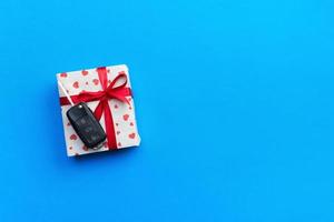 Car key on paper gift box with red ribbon bow and heart on blue table background. Holidays present top view concept photo