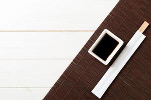 Bamboo mat and soy sauce with sushi chopsticks on white wooden table. Top view with copy space background for sushi. Flat lay photo