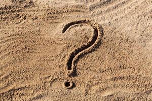 question marks written on beach sand close up, with copy space photo