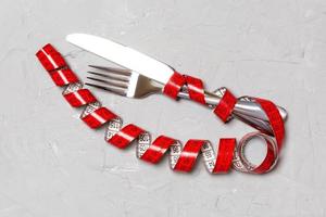 Diet concept with fork, knife and measuring tape on gray background. Top view of weight loss photo