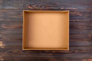 Opened brown blank cardboard box on wooden dark background, top view photo