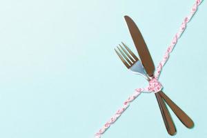 Diet and healthy eating concept with crossed fork and knife and curled measuring tape on blue background. Top view of weightloss with copy space photo