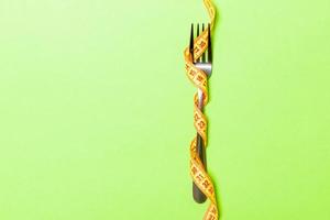 tenedor envuelto en cinta métrica sobre fondo verde. vista superior del concepto de comer en exceso