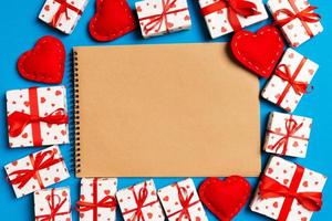 Top view of craft notebook surrounded with hearts and gift boxes on colorful background. Valentine's day photo