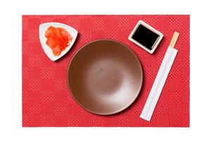 Empty round brown plate with chopsticks for sushi and soy sauce, ginger on red mat sushi background. Top view with copy space for you design photo