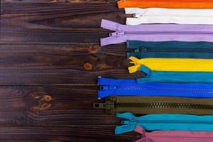 Multicolored zippers are laid out on a wooden table photo