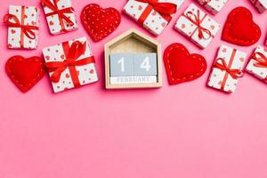 Top view of gift boxes, wooden calendar and red textile hearts on colorful background. The fourteenth of february. St Valentine's day concept with copy space photo