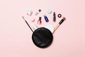 Vista superior de la bolsa de cosméticos con productos de maquillaje derramados sobre fondo rosa. concepto de belleza con espacio vacío para tu diseño foto