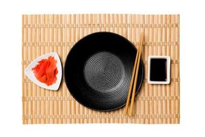 Empty round black plate with chopsticks for sushi and soy sauce, ginger on yellow bamboo mat background. Top view with copy space for you design photo