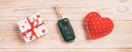 Valentine or other holiday handmade present in paper with red hearts, car keys and gifts box in holiday wrapper. box gift on orange wooden table top view with copy space, empty space for design photo