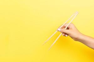 Girl's hand showing chopsticks on yellow background. Asian cuisine concept with empty space for your design photo