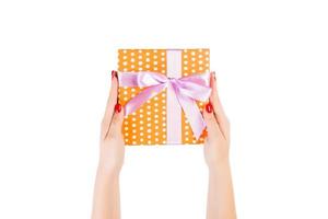 las manos de las mujeres dan Navidad envuelta u otro regalo hecho a mano en papel naranja con cinta morada. aislado sobre fondo blanco, vista superior. concepto de caja de regalo de acción de gracias foto