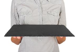 girl in the plaid shirt is holding an empty black square stone plate in front of her. woman hand hold empty dish for you desing. perspective view, isolated on white background photo