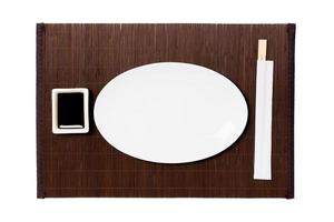 Empty oval white plate with chopsticks for sushi and soy sauce on dark bamboo mat background. Top view with copy space for you design photo