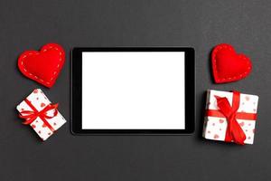 Top view of digital tablet surrounded with gift boxes and hearts on colorful background. Saint Valentine's day photo