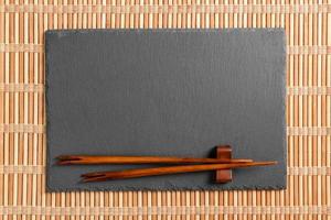 Empty rectangular black slate plate with chopsticks for sushi on wooden background. Top view with copy space photo