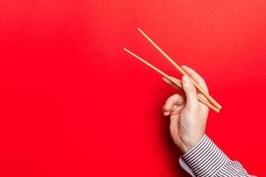 Male hand with chopsticks on red background. Traditional asian food with emty space for your design photo