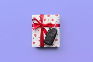 Give gift car key concept top view. Present box with red ribbon bow, heart and car key on purple colored background photo