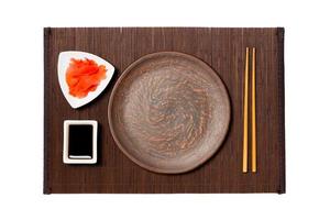 Empty round brown plate with chopsticks for sushi, ginger and soy sauce on dark bamboo mat background. Top view with copy space for you design photo