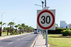 señal de límite de velocidad con panel solar en la carretera con palmera en un día de verano. el límite de velocidad es de 30 km h en un camino de grava foto