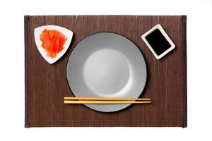 Empty round gray plate with chopsticks for sushi, ginger and soy sauce on dark bamboo mat background. Top view with copy space for you design photo