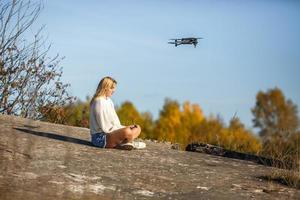 girl controls a drone sitting on high rock in the mountains photo