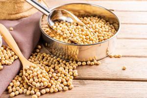 Soybean seeds in wooden bowl with wooden spoon, placed on wooden table, natural healthy food - top view. photo