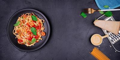 Delicious spaghetti pasta with prawns and cheese served on a black plate on a black background table Italian recipe, tomato sauce, vegetables, and spices top view with copy space photo