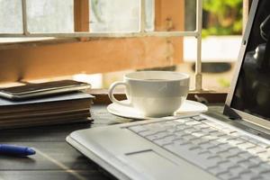 una taza de café con leche se coloca sobre el escritorio. oficina o en casa con un teclado de computadora portátil tablet pc foto