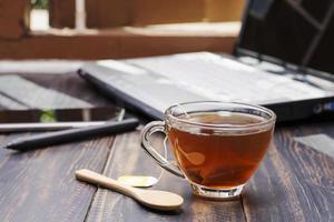 Close-up of a cup of hot tea or coffee placed on a desk with a computer. Or at a table for coffee by the window at work or home, at sunset or in the morning. photo