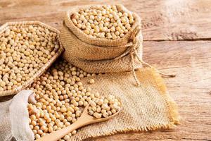 semillas de soja en una cuchara de madera y en un saco colocado sobre una mesa de madera semillas o alimentos saludables naturales - vista superior