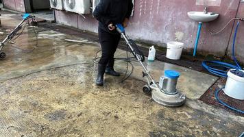 los empleados usan una fregadora de pisos de concreto en el estacionamiento de la oficina. casa u hotel limpie el piso exterior con un depurador y una solución química. servicios de negocios comerciales foto