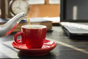 se coloca una taza de café roja sobre el escritorio. oficina o en casa con un teclado de computadora portátil tablet pc foto