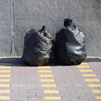 Two black garbage bags on tiled street floor at concrete fence in city photo