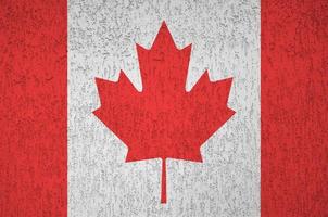 Canada flag depicted in bright paint colors on old relief plastering wall. Textured banner on rough background photo