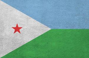 Djibouti flag depicted in bright paint colors on old relief plastering wall. Textured banner on rough background photo