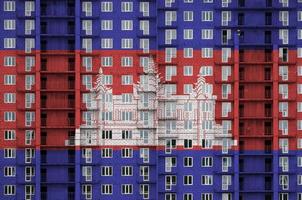 Cambodia flag depicted in paint colors on multi-storey residental building under construction. Textured banner on brick wall background photo