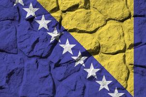 Bosnia and Herzegovina flag depicted in paint colors on old stone wall closeup. Textured banner on rock wall background photo