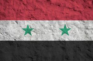 Syria flag depicted in bright paint colors on old relief plastering wall. Textured banner on rough background photo