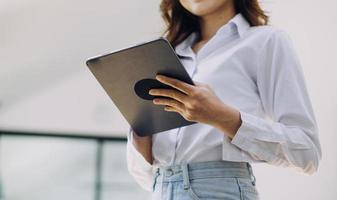 Young business woman sitting in office at table and using smartphone. On desk is laptop and tablet computer, on screen charts and graphs. Woman analyzing data. Student learning online. photo