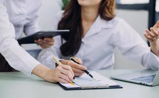 Young business woman sitting in office at table and using smartphone. On desk is laptop and tablet computer, on screen charts and graphs. Woman analyzing data. Student learning online. photo