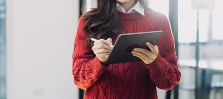 Young business woman sitting in office at table and using smartphone. On desk is laptop and tablet computer, on screen charts and graphs. Woman analyzing data. Student learning online. photo