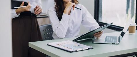 Young business woman sitting in office at table and using smartphone. On desk is laptop and tablet computer, on screen charts and graphs. Woman analyzing data. Student learning online. photo