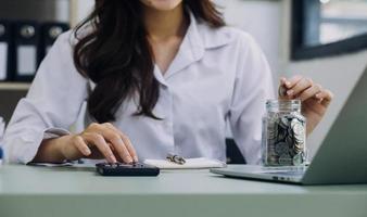 Young business woman sitting in office at table and using smartphone. On desk is laptop and tablet computer, on screen charts and graphs. Woman analyzing data. Student learning online. photo
