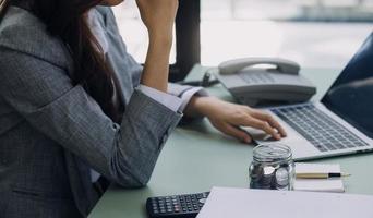 Young business woman sitting in office at table and using smartphone. On desk is laptop and tablet computer, on screen charts and graphs. Woman analyzing data. Student learning online. photo