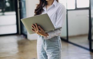 Young business woman sitting in office at table and using smartphone. On desk is laptop and tablet computer, on screen charts and graphs. Woman analyzing data. Student learning online. photo