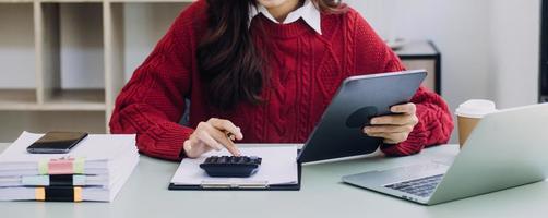 Young business woman sitting in office at table and using smartphone. On desk is laptop and tablet computer, on screen charts and graphs. Woman analyzing data. Student learning online. photo