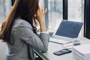Young business woman sitting in office at table and using smartphone. On desk is laptop and tablet computer, on screen charts and graphs. Woman analyzing data. Student learning online. photo