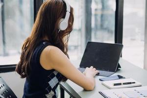 Young business woman sitting in office at table and using smartphone. On desk is laptop and tablet computer, on screen charts and graphs. Woman analyzing data. Student learning online. photo